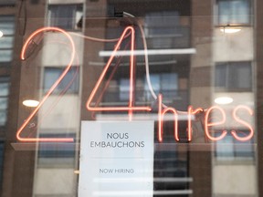 A neon sign says "24 hres." There is a help-wanted sign taped to the window.