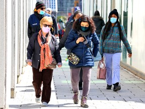 Masked pedestrians walk through the Quartiers des Spectacles in Montreal on April 11, 2022.