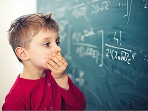 A boy looks at a math equation on a chalkboard. His hand is over his mouth and he looks overwhelmed.