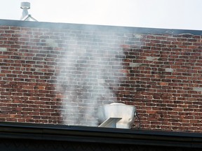 Smoke comes out of a rooftop exhaust pipe