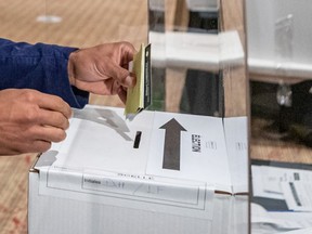 A voter places a ballot in a municipal election ballot box.