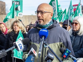 Réjean Leclerc speaks into news media microphones surrounded by union activists with flags