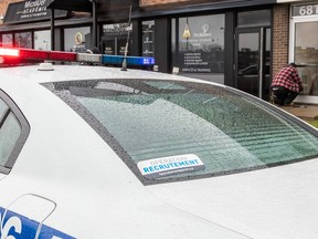 A worker replaces broken glass on the front door at the Jewish Community Council of Montreal after it was hit by a Molotov cocktail on Nov. 27, 2023 as a police car is parked out front..