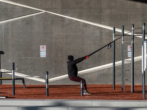 A man in winter clothing pulls on tension straps attached to exercise apparatus near a concrete wall outside