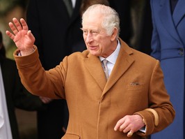 king charles is waving. he is wearing a brown overcoat.