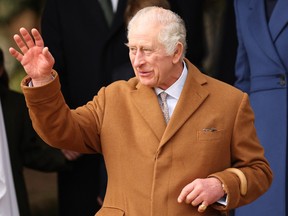 King Charles is waving. He is wearing a brown overcoat.