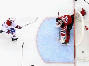 An overhead shot shows the puck in the net behind the New Jersey goaltender as a Canadiens player skates in front of the crease