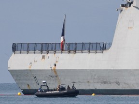 A small motorboat is seen next to a large ship with a French flag on its deck