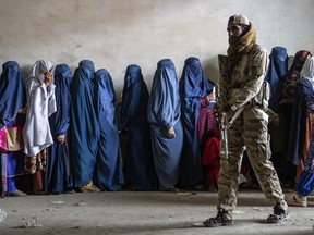 A Taliban fighter stands guard as women wait to receive food rations distributed by a humanitarian aid group, in Kabul, Afghanistan, on May 23, 2023.