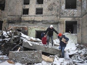 People walk with belongings from an apartment building destroyed after Tuesday's Russian attack in Kyiv, Ukraine, Wednesday, Jan. 3, 2024.