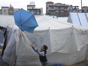 A Palestinian boy displaced by the Israeli bombardment plays with an umbrella outside a makeshift tent in Rafah, Gaza Strip, Tuesday, Jan. 2, 2023.