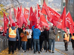 Teachers walk a picket line with large red flags that have the FAE union logo.