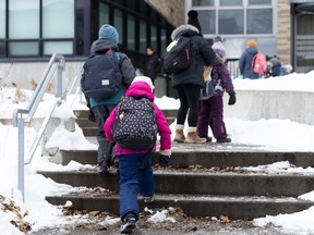 Children in winter clothing walk up the stairs to a school.