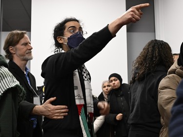 A man wearing a face mask and a red white and green scarf points at something while another person puts a hand on his side