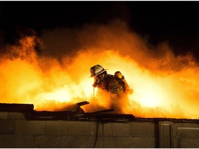 A firefighter fights a fire on the roof of a building at night