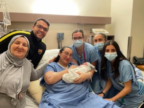 Mother holds her newborn baby surrounded by her husband and hospital staff exactly at midnight on New Year's Day.
