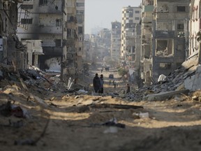 Palestinians walk between the remains of destroyed buildings following the Israeli bombardment on the main road of Gaza City on Tuesday, Jan. 2, 2024.