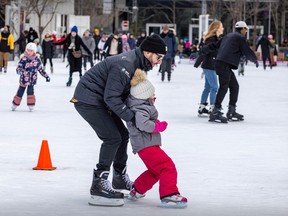 A father holds up his young daughter on a crowded outdoor skating rink