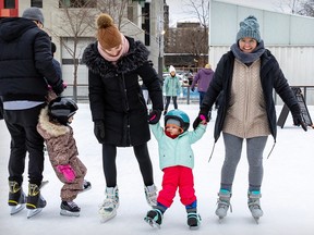 Two adults hold up a small girl on an outdoor skating rink