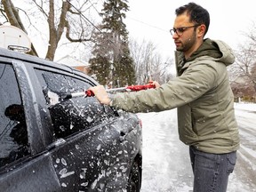 A man scrapes ice off the side window of a car.