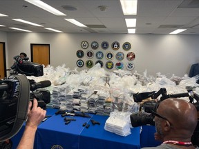 Cameras are seen taking picture of tables with seized drugs, money and weapons on them.