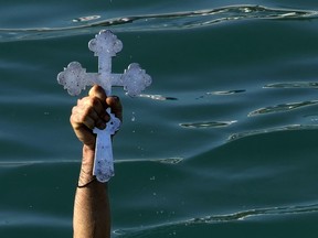 A pilgrim holds up the crucifix after it was thrown into the water by an Orthodox priest.