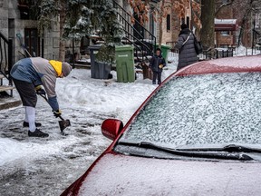 A man shovels ice from a walkway. In the foreground is an ice-covered car.