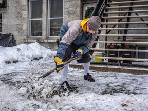 A man shovels ice from a walkway at the bottom of wooden stairs.
