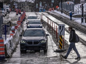 A man crosses a street in front of a row of cars navigating construction on a wet road.