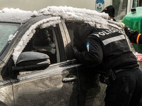 A police officer peers through the window of a snow-covered car.