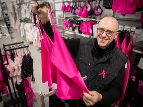 A man in a lingerie shop holds up a pink camisole.