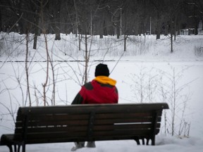 A person sits on a bench overlooking a snow-covered pond.
