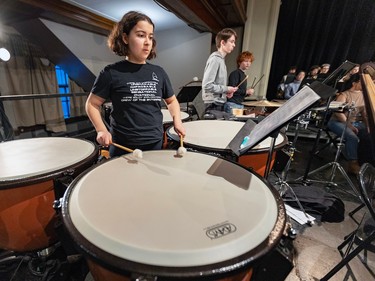 A girl plays drums with other percussionists in the background.