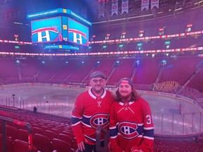 A father and son in Canadiens jerseys pose in the stands of a near-empty Bell Centre, with the scoreboard in the background.