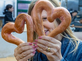 A woman is holding up two heart-shaped bagels and one of her eyes is peeking out the right one.