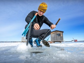 A man crouches over a hole in the ice on a sunny day.