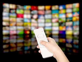 A person is holding a white remote. In the blurred background are many colourful squares.