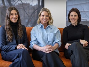 Three women smile while posing for a picture on a couch