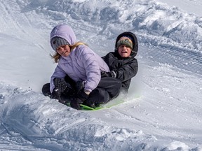 Two children laugh as they slide on a plastic sled.