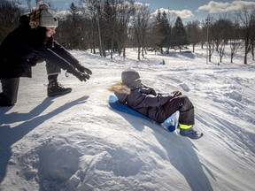 A child pushes another down a snowy hill on a plastic sled.