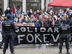 Two police officers stand in front of a group holding a large sign reading 'solidarite forever' outside a building