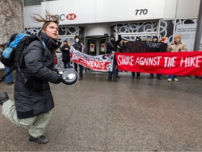 A young woman dances and bangs a pot in front of students holding signs reading Strike Against the Hike and other slogans, outside an HSBC building.