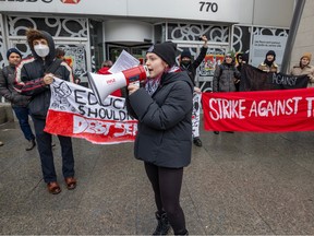 A woman speaks into a megaphone while protesters hold up banners behind her outside a building