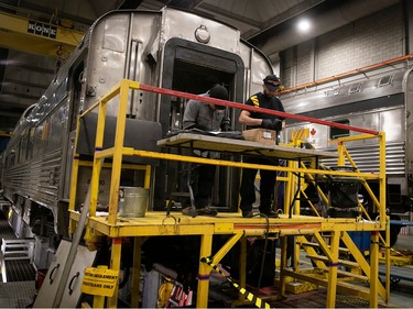 Two workers on a platform next to the end of a rail car in a maintenance building