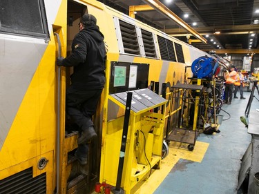 A worker climbs into the cab of a yellow locomotive in a maintenance building