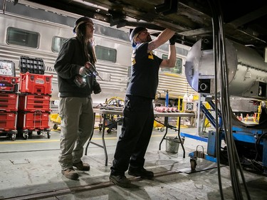 Two workers stand underneath a train car performing maintenance