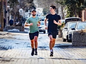 Two men dressed in t-shirts and shorts run along a cobblestone street in winter