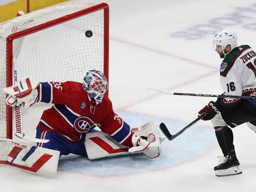 A puck flies over the head of Canadiens' goaltender Sam Montembeault with Coyotes' Jason Zucker in front of the crease