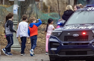 A young boy salutes a police officer as he and other students walk down the sidewalk.