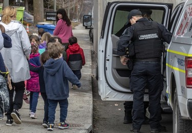 A paramedic stands in the doorway of his vehicle as children file past on the sidewalk.